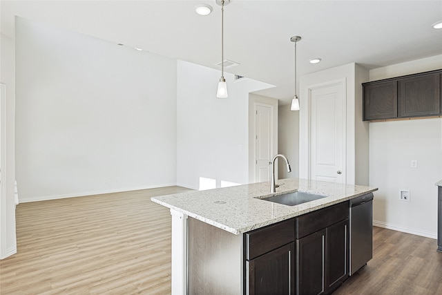 kitchen featuring light stone countertops, dishwasher, sink, pendant lighting, and a center island with sink