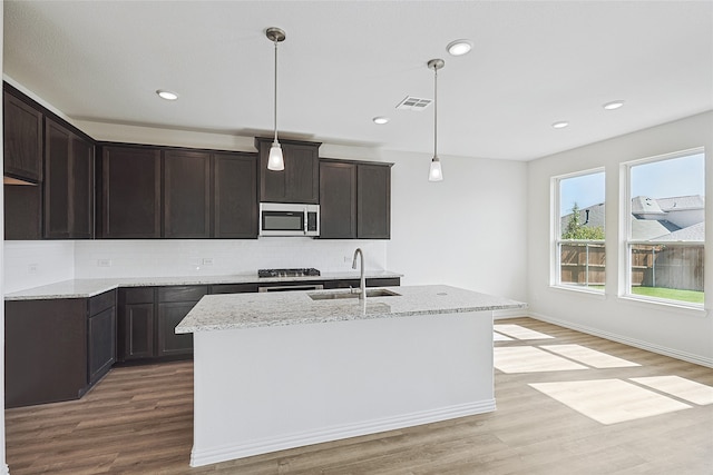 kitchen with pendant lighting, an island with sink, sink, light wood-type flooring, and dark brown cabinets