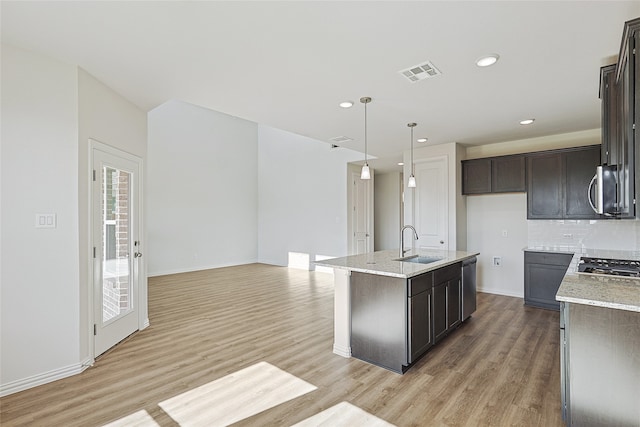 kitchen with sink, light stone countertops, a kitchen island with sink, and pendant lighting