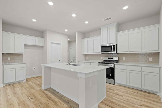 kitchen with white cabinetry, sink, a kitchen island with sink, light hardwood / wood-style floors, and stainless steel appliances