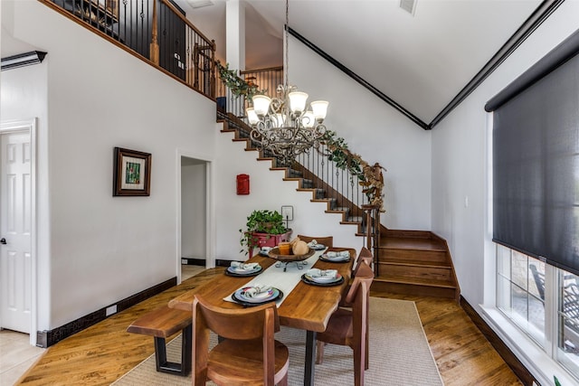 dining room featuring crown molding, a towering ceiling, a chandelier, and light hardwood / wood-style floors