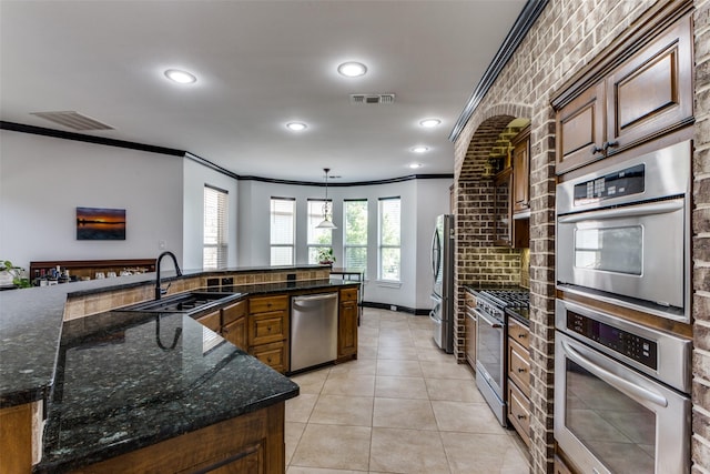 kitchen featuring sink, appliances with stainless steel finishes, dark stone countertops, ornamental molding, and decorative light fixtures