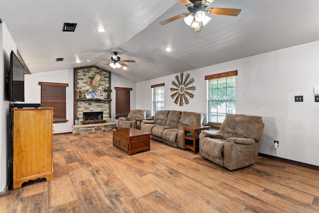 living room featuring ceiling fan, light hardwood / wood-style floors, a stone fireplace, and vaulted ceiling