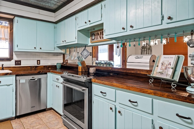 kitchen featuring wood counters, stainless steel appliances, sink, blue cabinetry, and light tile patterned flooring