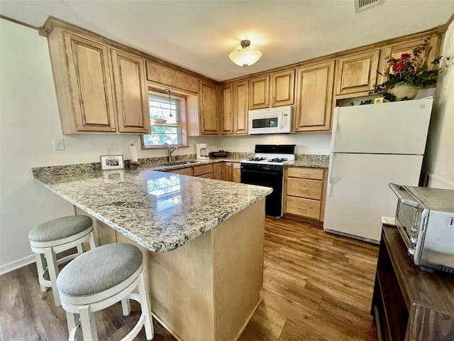 kitchen with a kitchen bar, light hardwood / wood-style floors, kitchen peninsula, white appliances, and light stone counters