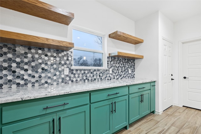 kitchen with tasteful backsplash, light stone countertops, green cabinets, and light hardwood / wood-style flooring