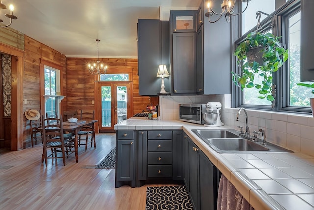 kitchen featuring tile counters, sink, wooden walls, light hardwood / wood-style flooring, and decorative backsplash