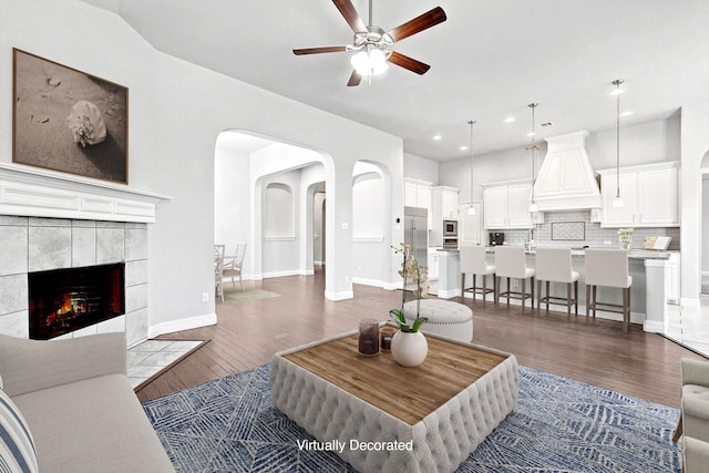 living room with ceiling fan, dark hardwood / wood-style floors, and a tiled fireplace