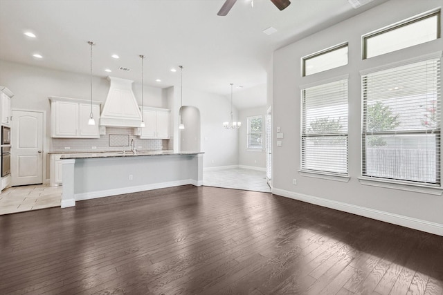 unfurnished living room with ceiling fan with notable chandelier, sink, and hardwood / wood-style floors