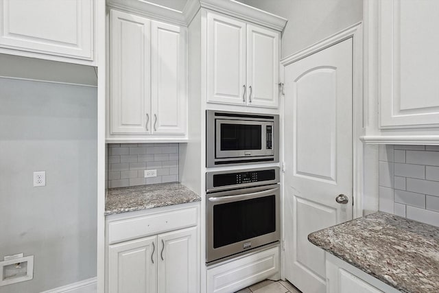 kitchen with light tile patterned floors, dark stone counters, stainless steel appliances, decorative backsplash, and white cabinets