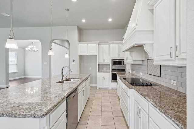 kitchen with sink, light stone counters, hanging light fixtures, appliances with stainless steel finishes, and an island with sink