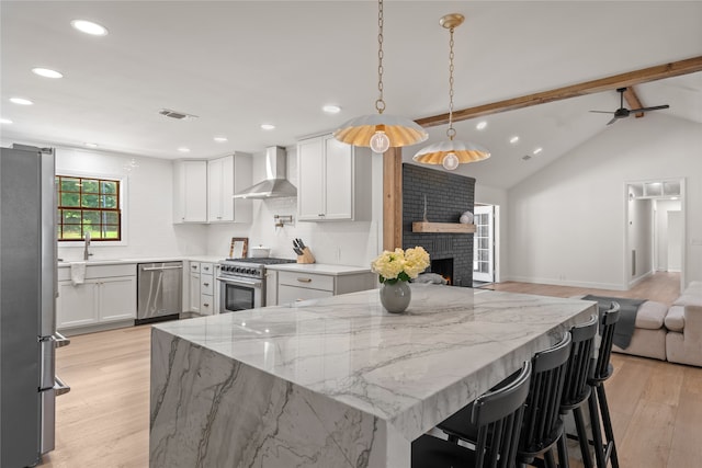 kitchen with backsplash, hanging light fixtures, wall chimney exhaust hood, appliances with stainless steel finishes, and white cabinetry