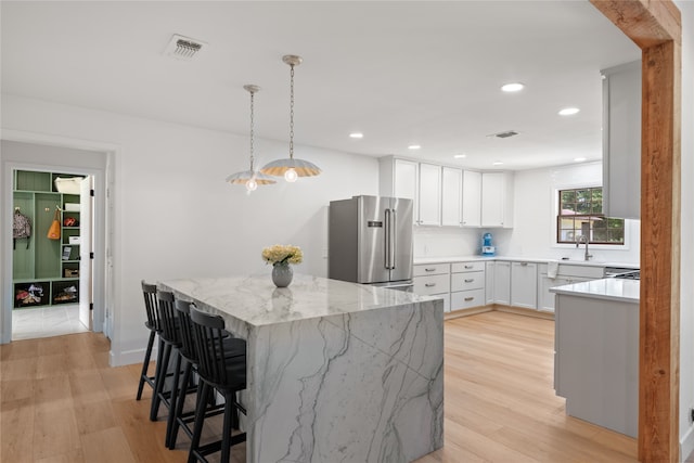 kitchen with pendant lighting, high end fridge, light stone countertops, and white cabinetry