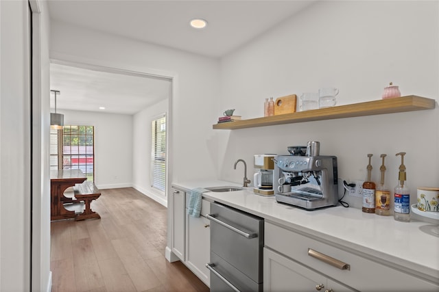 kitchen with white cabinetry, sink, dishwasher, decorative light fixtures, and light wood-type flooring