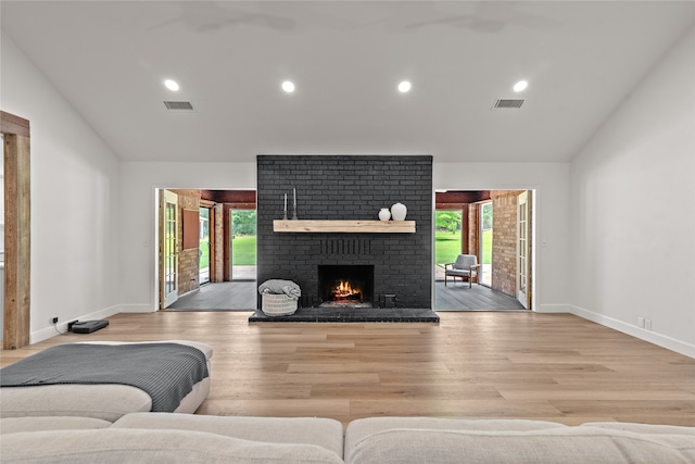 living room with vaulted ceiling, light wood-type flooring, and a brick fireplace