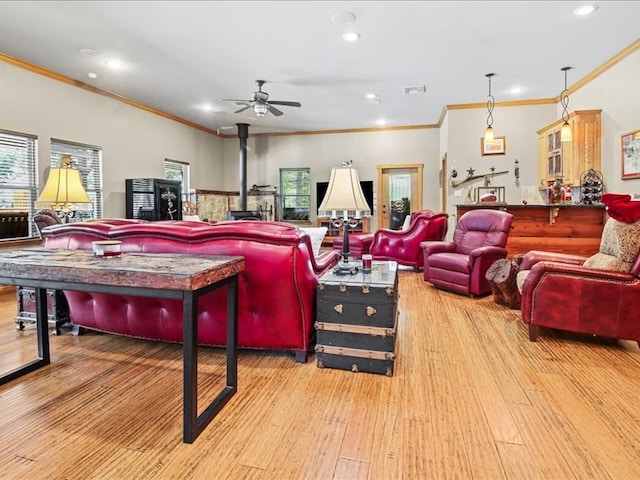 living room featuring ornamental molding, ceiling fan, a wood stove, and light hardwood / wood-style flooring