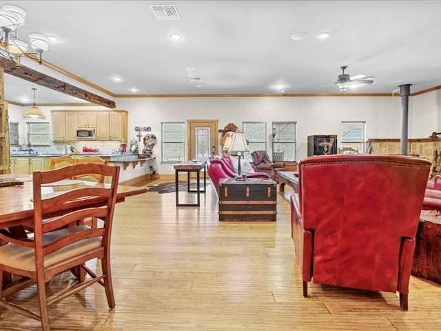 living room featuring ornamental molding, light wood-type flooring, a wood stove, and ceiling fan