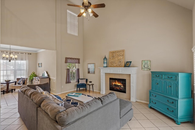 living room featuring a towering ceiling, a tiled fireplace, ceiling fan with notable chandelier, and light tile patterned floors