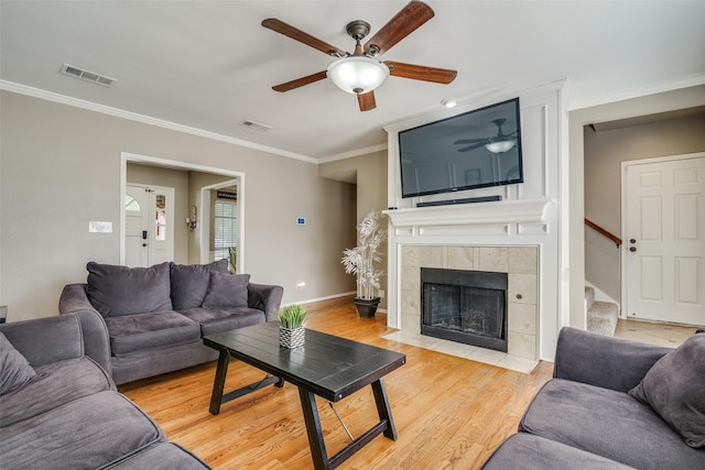 living room with ceiling fan, crown molding, light wood-type flooring, and a fireplace