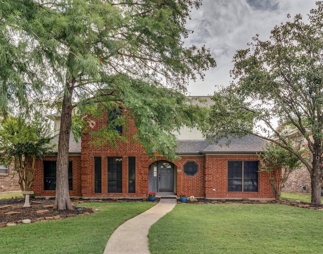 traditional-style home with brick siding, a shingled roof, and a front yard