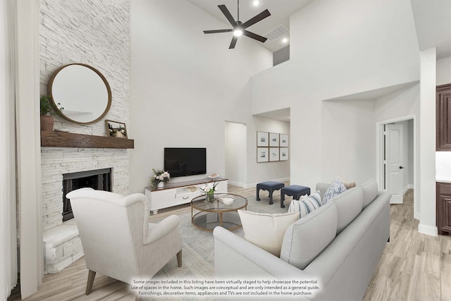 living room with light hardwood / wood-style flooring, ceiling fan, a stone fireplace, and high vaulted ceiling