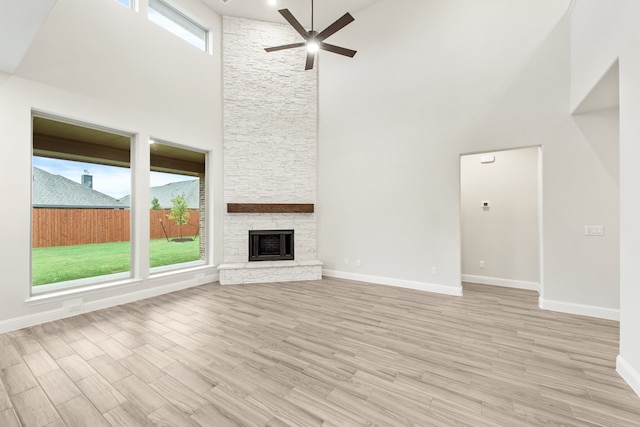 unfurnished living room with high vaulted ceiling, a fireplace, light hardwood / wood-style floors, and ceiling fan