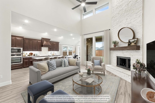 living room with light hardwood / wood-style flooring, ceiling fan, a high ceiling, and a fireplace