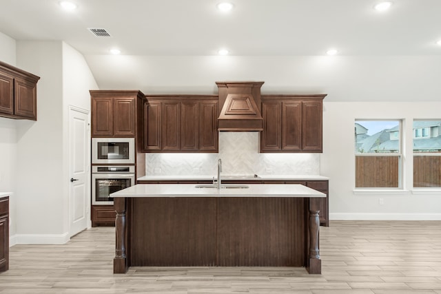 kitchen with an island with sink, sink, oven, and light hardwood / wood-style floors