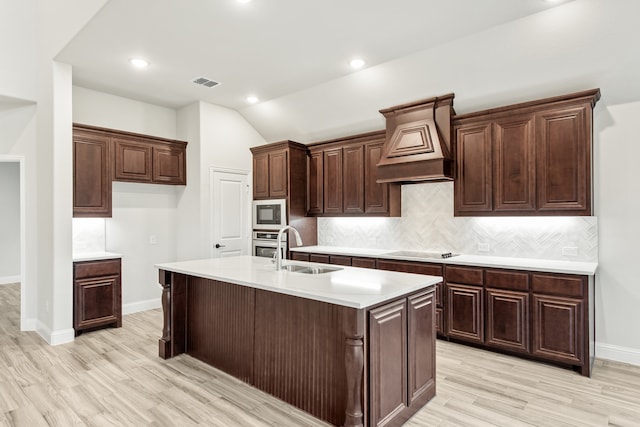 kitchen featuring lofted ceiling, dark brown cabinets, and a kitchen island with sink