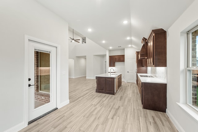 kitchen with light hardwood / wood-style floors, sink, black electric cooktop, ceiling fan, and a kitchen island with sink