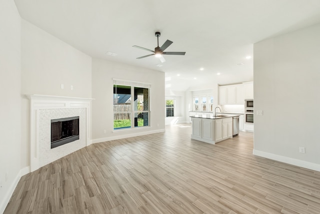 unfurnished living room with ceiling fan, light wood-type flooring, and sink