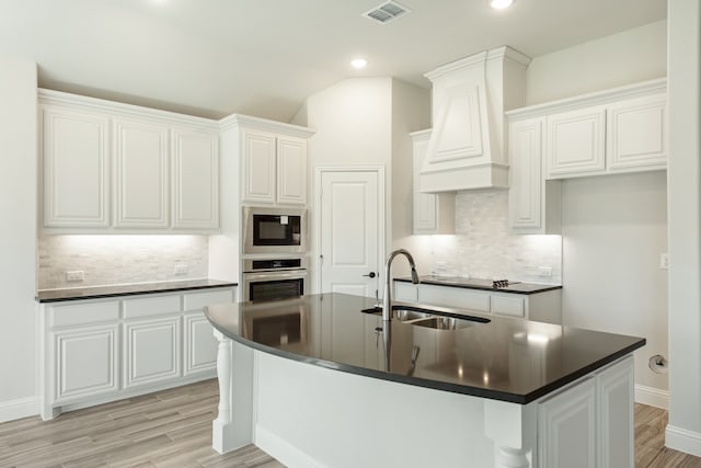 kitchen featuring decorative backsplash, stainless steel oven, an island with sink, and white cabinets