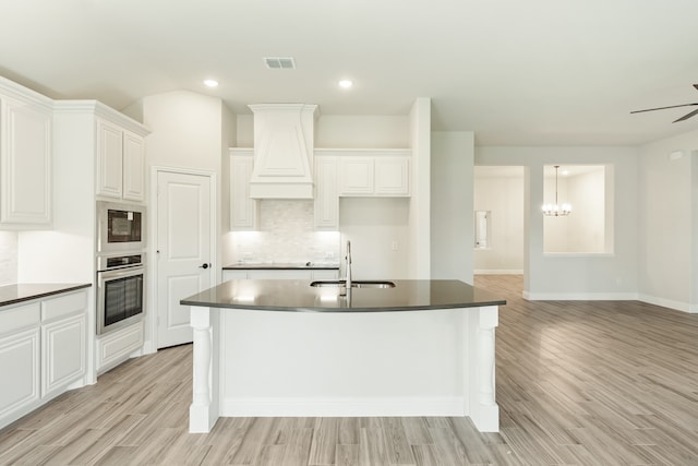 kitchen with light wood-type flooring, a center island with sink, white cabinetry, and sink