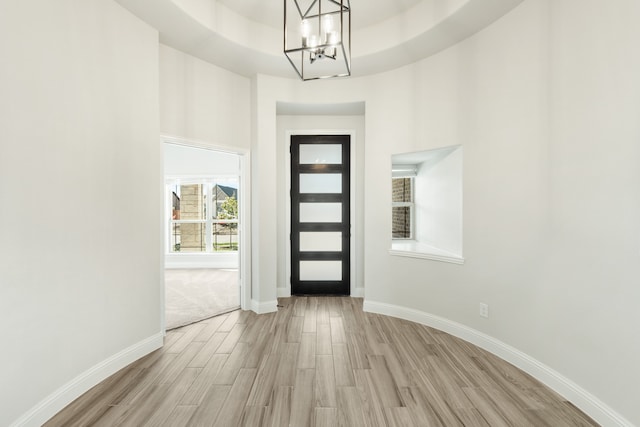 entrance foyer featuring light wood-type flooring, a raised ceiling, a high ceiling, and a notable chandelier