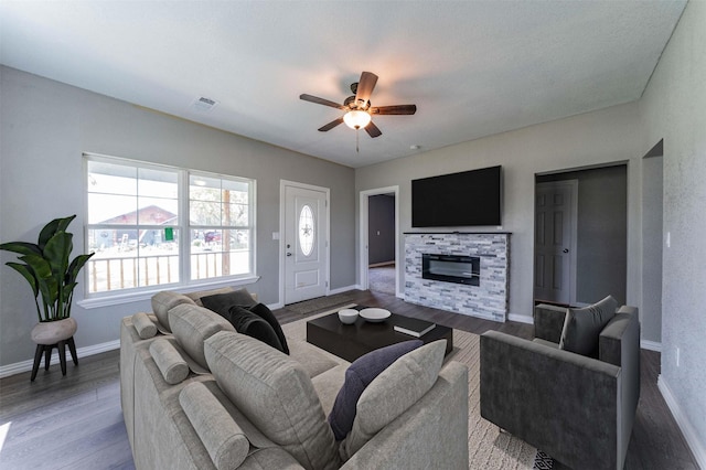 living room featuring hardwood / wood-style flooring, ceiling fan, and a stone fireplace