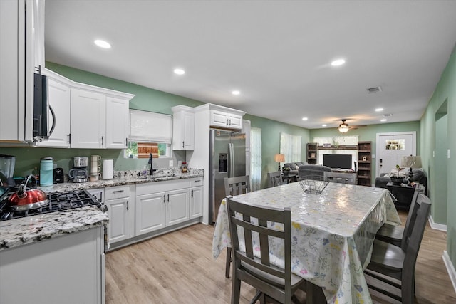 kitchen with light stone countertops, white cabinets, sink, stainless steel fridge, and ceiling fan