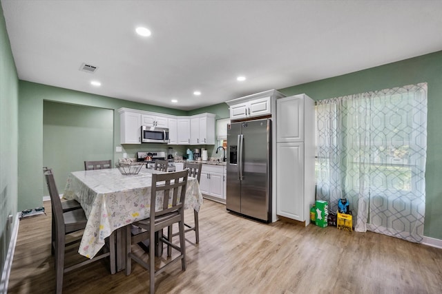 kitchen with white cabinets, light wood-type flooring, a breakfast bar, and stainless steel appliances