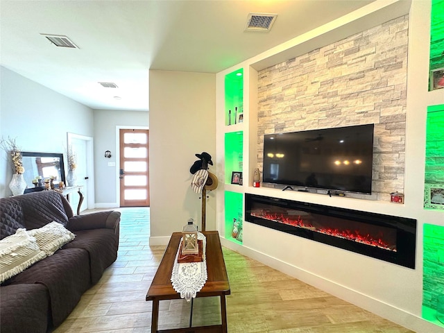 living room with wood finished floors, a glass covered fireplace, and visible vents