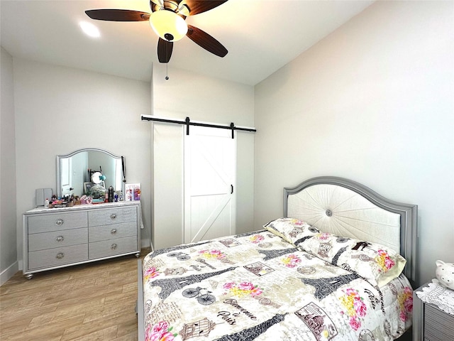 bedroom with light wood-type flooring, ceiling fan, and a barn door