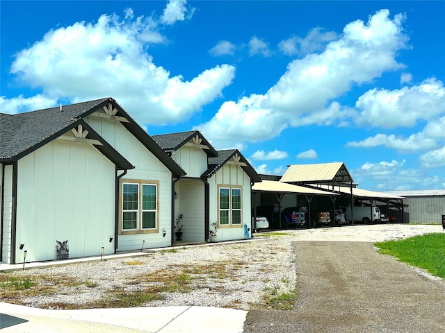 modern inspired farmhouse with board and batten siding, roof with shingles, driveway, and a carport