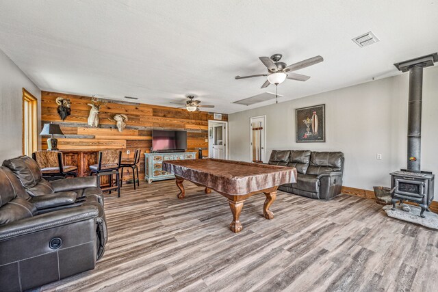 game room featuring ceiling fan, wood-type flooring, rustic walls, a wood stove, and billiards