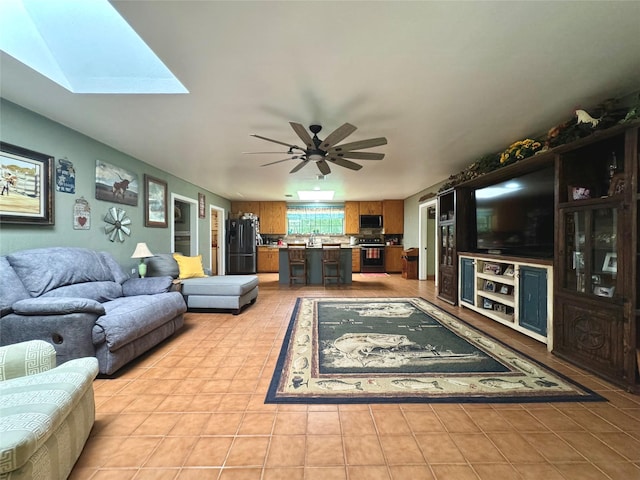 living area featuring light tile patterned flooring, a skylight, and a ceiling fan