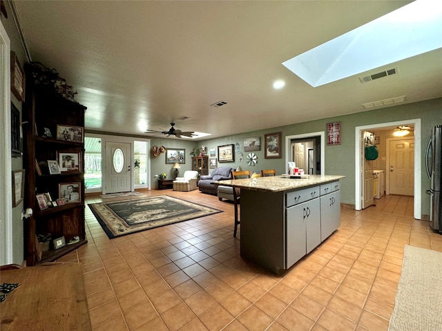 kitchen with ceiling fan, light tile floors, a center island, a skylight, and stainless steel refrigerator