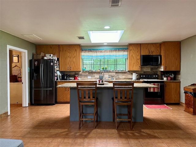 kitchen with black appliances, backsplash, a kitchen island, and a skylight