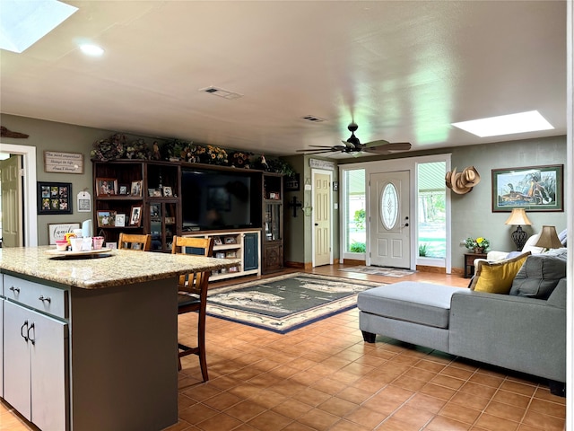 living room featuring light tile floors, ceiling fan, and a skylight