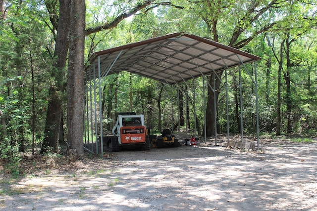 view of parking / parking lot featuring a carport, gravel driveway, and a forest view