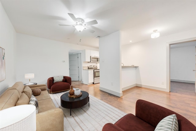 living room with visible vents, light wood-type flooring, a ceiling fan, and baseboards