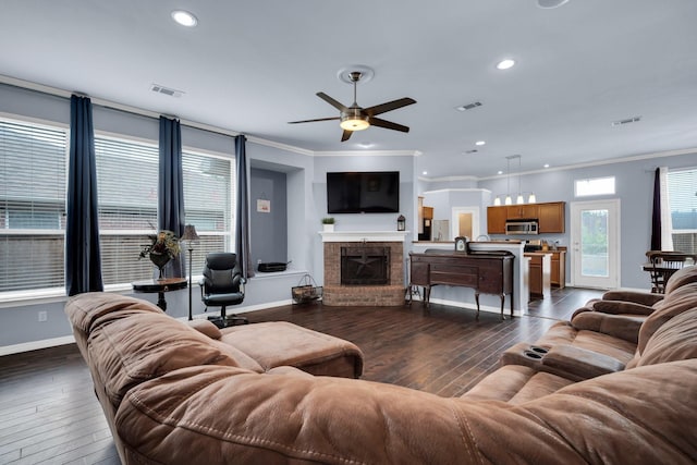 living room featuring ceiling fan, dark hardwood / wood-style flooring, crown molding, and a brick fireplace