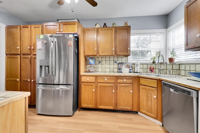 kitchen with appliances with stainless steel finishes, backsplash, ceiling fan, sink, and light hardwood / wood-style flooring