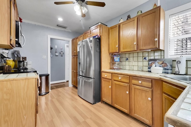 kitchen with tile countertops, sink, light wood-type flooring, and stainless steel refrigerator with ice dispenser